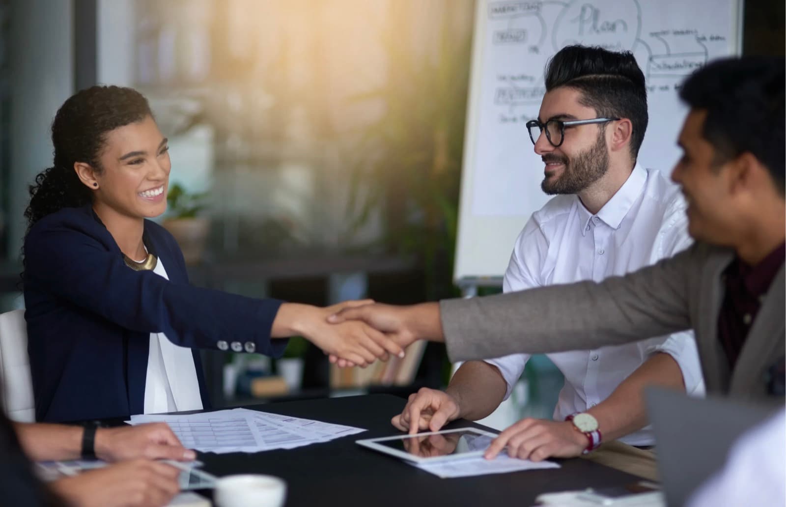 Two people shaking hands across a conference table at the end of a client meeting